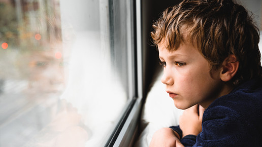 Foto: Ein Kind schaut schaut traurig aus dem Fenster