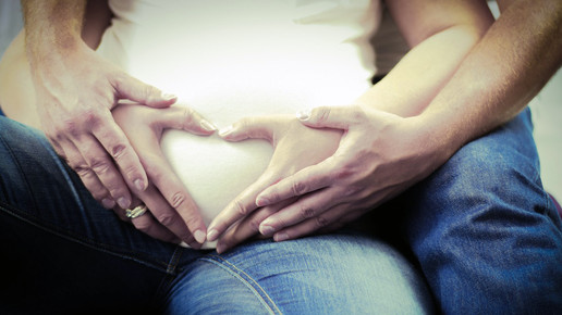 Symbolbild: schwangeres Pärchen, das mit den Händen ein Herz auf ihrem Babybauch formt