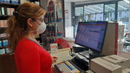 PTA mit Maske hinter Plexiglas hinter dem HV. Vor ihr ein Computer und eine Tastatur.