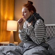 Atemwegsinfekte: Phytotherapie statt Antibiotika Foto: Eine Person sitzt zugedeckt mit Schal im Bett und hustet