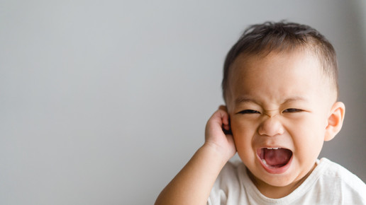 Baby schreit und fasst sich ins Gesicht.