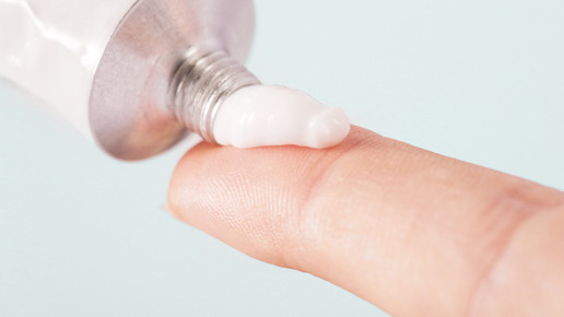 Foto: Creme wird aus einer Aluminiumtube auf eine Fingerkuppe gedrückt.