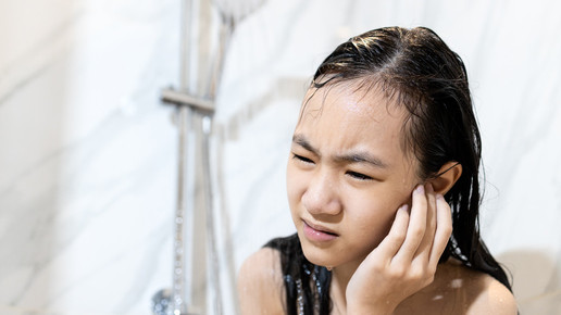 Mädchen hält sich schmerzendes Ohr beim duschen.