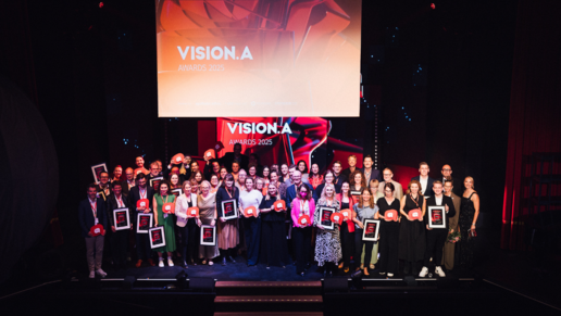 Gruppenbild auf der Bühne des Wintergarten Varieté Berlin: Alle Gewinnerinnen und Gewinner des Abends posieren mit ihren VISION.A Trophäen vor Vorhängen und Scheinwerfern, stolz in die Kamera.