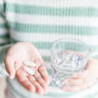 Opioide erhöhen Krebsrisiko Foto: Eine Person hält Kapseln in der einen und ein Wasserglas in der anderen Hand.
