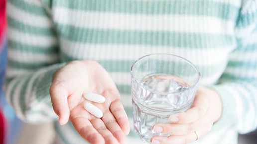 Foto: Eine Person hält Kapseln in der einen und ein Wasserglas in der anderen Hand.