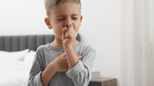 Foto: Ein Junge hustet und hält sich die Hand vor den Mund.