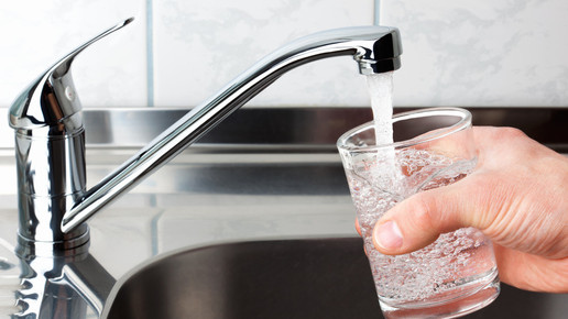 Symbolbild: Person füllt ein Glas Wasser an der Spüle 