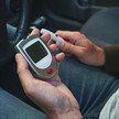 Diabetes im Straßenverkehr: Erhöhtes Unfallrisiko überholt? Foto: Eine Person hält ein Blutzuckermessgerät in der Hand, während sie im Auto sitzt