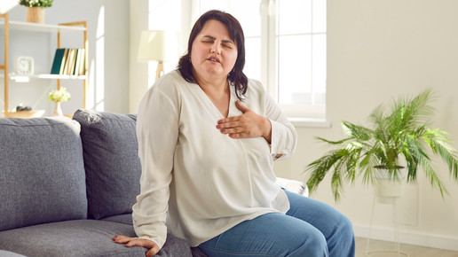 Foto: Eine übergewichtige Person sitzt auf einer Couch und berührt ihre Herzregion
