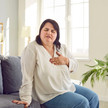 Semaglutid: Herzschutz unabhängig von Gewichtsverlust Foto: Eine übergewichtige Person sitzt auf einer Couch und berührt ihre Herzregion