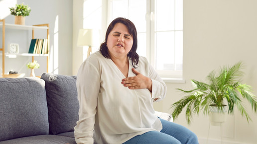Foto: Eine übergewichtige Person sitzt auf einer Couch und berührt ihre Herzregion