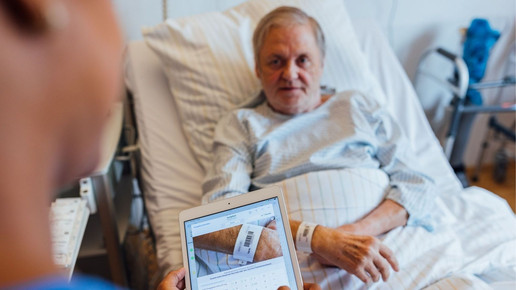 Pflegekraft scannt mit Tablet den Strichcode auf dem Armband eines Patienten