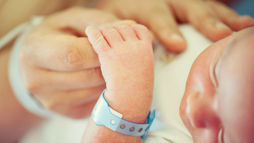 Baby mit Armband hält die Hand eines Erwachsenen
