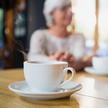 Demenz: Koffein bremst kognitiven Verfall Foto: Zwei ältere Personen im Hintergrund, im Vordergrund fokussiert eine Tasse Tee/Kaffee
