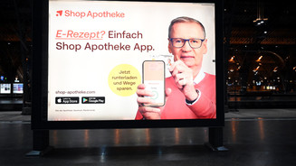 Das Foto zeigt ein Werbeplakat des Versenders ShopApotheke. TV-Moderator Günther Jauch hält ein Handy hoch, auf dem die ShopApotheke-App geöffnet ist. Er hält eine Gesundheitskarte von hinten an das Gerät. Auf dem Plakat steht: „E-Rezept? Einfach ShopApotheke-App. Jetzt herunterladen und Wege sparen.“
