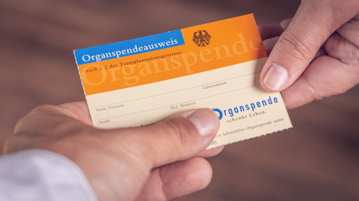 Foto: Eine Person reicht einer anderen Person einen Organspendeausweis.