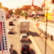 RKI: Fast 10.000 hitzebedingte Todesfälle Symbolbild: Das Foto zeigt im Vordergrund ein Thermometer. Im Hintergrund ist eine sonnenbeschienene, mehrspurige und stark befahrene Straße zu sehen.