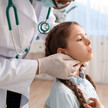 Foto: Eine Person mit Stethoskop im Kittel tastet den Hals eines Kindes ab