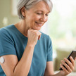 eine ältere Frau mit CGM-Sensor am Arm checkt ihre Werte am Handy