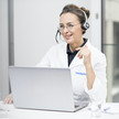 Eine Medgate-Ärztin im weißen Kittel und mit Headset sitzt vor einem Laptop. 