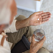 Foto: Eine ältere Person mit einem Glas Wasser und einer Tablette