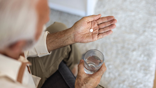 Foto: Eine ältere Person mit einem Glas Wasser und einer Tablette