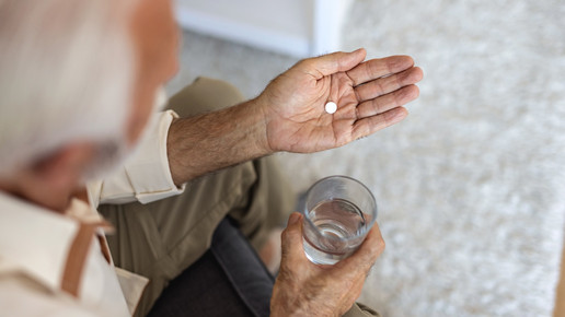 Foto: Eine ältere Person mit einem Glas Wasser und einer Tablette