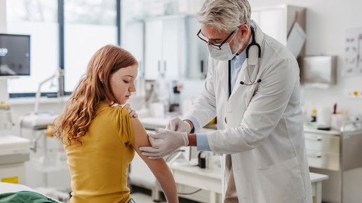 Foto: Ein Mann mit Mundschutz und weißem Kittel impft ein Mädchen.