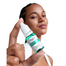 Eine junge Frau hält ein kleines Eucerin Dermopure Fläschchen nah an die Kamera.
