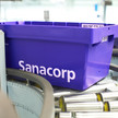 Eine blaue Sanacorp-Wanne fährt über das Förderband. Mehr dazu im Artikel.