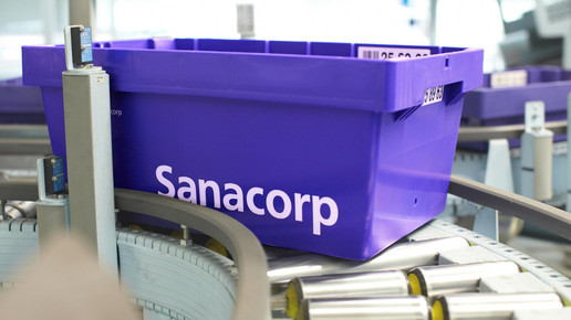 Eine blaue Sanacorp-Wanne fährt über das Förderband. Mehr dazu im Artikel.