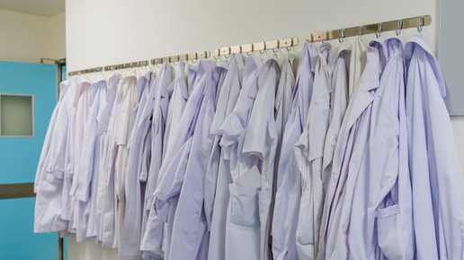 Wand mit vielen Haken an denen zahlreiche Kittel nebeneinander hängen.