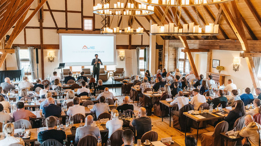Philipp Kohl steht mit Mikrofon auf einer Bühne und spricht zu einem Publikum aus Apothekerinnen und Apothekern, die in einem hellen Tagungsraum sitzen. Im Hintergrund sind Banner mit dem AVIE-Logo zu sehen