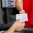 Foto: Eine Person reicht einer anderen Person ein Muster-16-Rezept in einer Apotheke