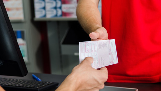 Foto: Eine Person reicht einer anderen Person ein Muster-16-Rezept in einer Apotheke