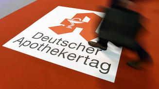Symbolbild: Roter Teppich mit rotem Apotheken „A“ auf weißem Grund und der Aufschrift „Deutscher Apothekertag“, eine Person geht mit schnellem Schritt darüber. 