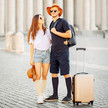 Die Abbildung zeigt ein junges Pärchen. Sie ist angezogen mit einer kurzen Jeans und einen weißen T-Shirt, hat einen Sommerhut in der Hand. Er ist ganz in dunkelblau angezogen, T-Shirt, kurze Hose. Sie tragen beide Reise Kniestrümpfe, vor ihnen steht ein Koffertrolley.