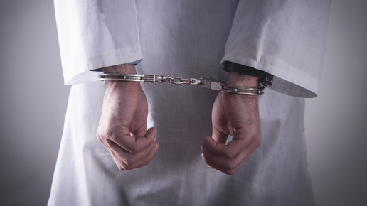 Symbolfoto: Rückansicht einer Person in weißem Kittel, mit Handschellen.