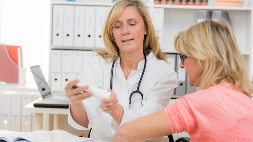 Foto: Eine Ärztin zeigt ihrer Patientin eine Creme- oder Salbentube.