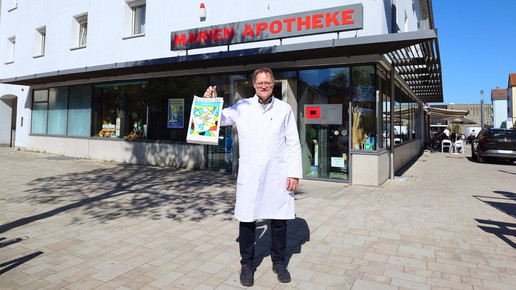 Foto: Inhaber Heinrich Hallatschek hält eine Überraschungstüte für Too Good To Go vor seiner Apotheke hoch