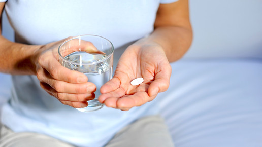 Foto: eine Person hält ein Glas Wasser in der rechten, eine Tablette in der linken Hand