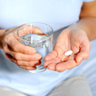 Foto: eine Person hält ein Glas Wasser in der rechten, eine Tablette in der linken Hand