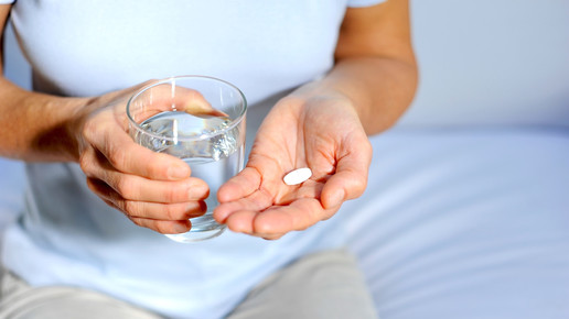 Foto: eine Person hält ein Glas Wasser in der rechten, eine Tablette in der linken Hand