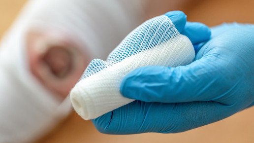 Foto: Unscharf im Hintergrund eine chronische Wunde, die mit einem Verband versorgt wird.