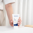 Nahaufnahme einer Hand, die die DERMASENCE Adtop Handcreme (50 ml) auf einem weißen Tisch hält, vor hellem, minimalistischem Hintergrund.