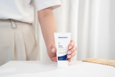 Nahaufnahme einer Hand, die die DERMASENCE Adtop Handcreme (50 ml) auf einem weißen Tisch hält, vor hellem, minimalistischem Hintergrund.