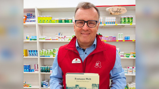 Dr. Thomas Richter in seiner Apotheke, hält ein Fontane-Buch hoch