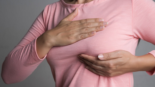 Foto: Eine weibliche Person in einem rosafarbenen Oberteil tastet sich die linke Brust ab