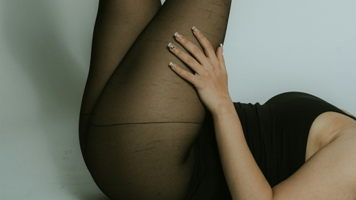 Weibliche Beine in schwarzer, halbblickdichter Strumpfhose in die Luft gestreckt.